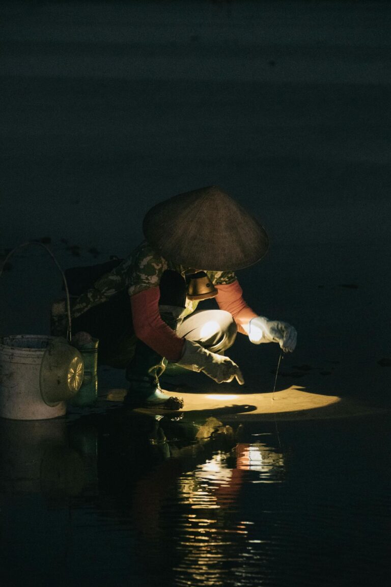 A fisherman uses a light to harvest clams from water at twilight, showcasing traditional methods.