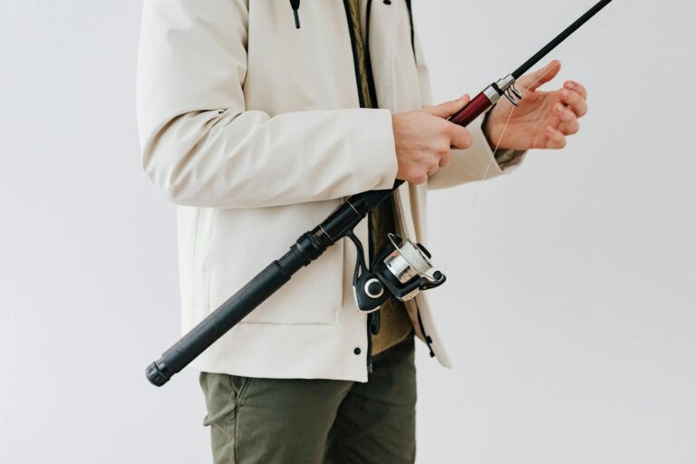Detail of a person wearing a jacket and holding a fishing rod, emphasizing fishing equipment.